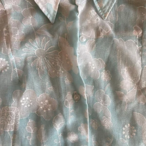 Blommig blus i ljusblått - Säljer en söt ljusblå blus med blommigt mönster. Blusen har långa ärmar och knappar framtill. 90-tal. Inga anmärkningar💕