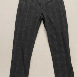 Svarta byxor från Zara - Snygga svarta kostymbyxor från Zara med diskret rutmönster. Byxorna har en klassisk passform med knappar och dragkedja framtill. Perfekta för en stilren look. Slim/skinny fit 