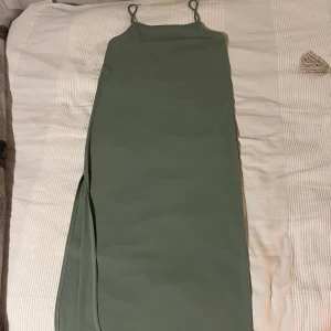 Grön midiklänning från H&M - Snygg grön midiklänning från H&M med smala axelband och en slit på sidan. Har varit insydd på sidorna då den var för stor för mig, så det finns små märken där sömmarna suttit men syns inte då man har på sig den😊