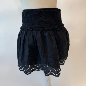 Svart kjol med broderad kant - Snygg svart kortkjol med elastisk midja och vacker broderad kant. Perfekt för en stilren look med en touch av elegans.