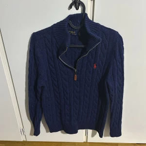 Mörk Blå stickad tröja från Polo Ralph Lauren - Säljer en snygg blå stickad tröja från Polo Ralph Lauren med dragkedja och broderad logga på bröstet. Helt ny, haft på mig den 1 gång men efter det har jag gått upp i vikt och den har blivit för liten på mig och det är därför jag säljer den.