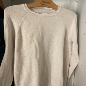 Vit stickad tröja - Säljer en stilren vit stickad tröja med rund halsringning. Tröjan har långa ärmar och ribbade detaljer vid hals, ärmslut och nederkant. Perfekt för kyligare dagar.