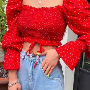 Röd blommig blus med puffärmar - Trendig röd blus med blommönster och puffiga långa ärmar. Den har en smockad design och en snygg passform. Perfekt för att liva upp garderoben!