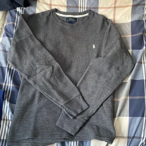 Grå långärmad tröja från Polo Ralph Lauren - Säljer en stilren grå långärmad tröja från Polo Ralph Lauren. Tröjan är tillverkad i 100% bomull och har en klassisk rund halsringning. Perfekt för en avslappnad och snygg look.