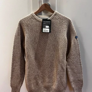 Beige stickad tröja från Pelle P - Säljer en stilren beige stickad tröja från Pelle P. Tröjan har en klassisk rund hals och långa ärmar med ribbade muddar. Perfekt för kyligare dagar. Helt oanvänd!Nypris 1100kr