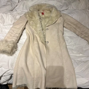 Päls kappa  - Säljer en elegant beige/benvit/creme vit  kappa från Esprit med fluffiga päls detaljer. Perfekt för kyliga dagar med sin stilrena design och mjuka material.