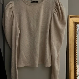Beige ribbad tröja från Zara - Säljer en stilren beige ribbad tröja från Zara med puffiga långa ärmar. Perfekt för en chic och elegant look. Tröjan har en rund halsringning och är i ett mjukt material.