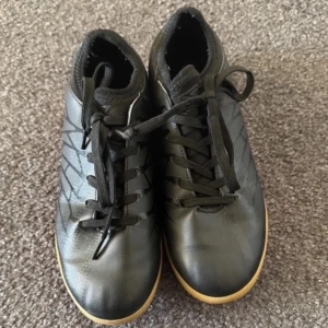 Svarta Umbro Inomhusskor fotboll med gummisula - Säljer ett par svarta fotbollsskor inomhus med snörning och slitstark gummisula. Perfekta för inomhusspel med en stilren design.