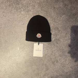 Svart Moncler mössa - Hej! Säljer denna snygga svarta mössan från Moncler med broderad logotyp framtill. Perfekt för kyliga dagar och en stilren look. Pris 800 kr