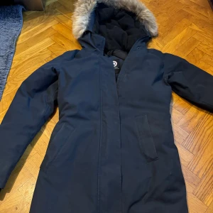 Canada Goose Victoria parka  - Canada Goose jacka i mörkblå färg. Jackan har en avtagbar huva med pälskant (avtagbar Äkta päls). Den har även en innerficka och två fickor på utsidan. Jackan är i utmärkt skick, perfekt för kalla vinterdagar. Kvitto kan jag skriva ut via Johnells sida som är digitalt , inköpt på Johnells(2023 oktober) 9900kr. Jag är även intresserad av att byta jackan mot en modell större (M) av samma märke Canada goose i BRA skick. Kan hämtas hos mig eller fraktas 