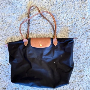 Svart och brun axelväska från Longchamp - Snygg svart axelväska från Longchamp med bruna skinnhandtag och lock. Perfekt för vardagsbruk med en stilren design och praktisk storlek.
