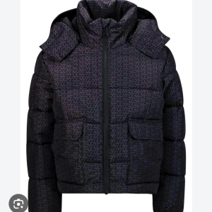 Pufferjacka från zadig  - Snygg svart pufferjacka med ett diskret mönster och praktisk huva. Jackan har dragkedja framtill och två fickor. Perfekt för kyliga dagar. Jackan är svart med lilablå zadig mönster. Skriv för egna bilder barnstorlek men passar xxs-xs