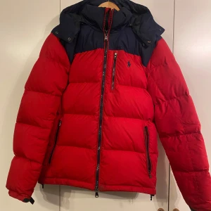 Röd och marinblå dunjacka från Polo Ralph Lauren - Snygg och varm röd dunjacka från Polo Ralph Lauren med marinblå detaljer. Den är i storlek S och använd fåtal gånger!!