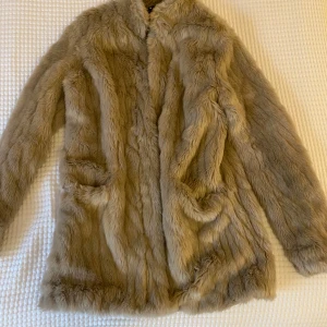 Beige pälsjacka - Säljer en fluffig och stilren beige pälsjacka med långa ärmar. Perfekt för att hålla sig varm och trendig under kyliga dagar. Jackan har en klassisk design som passar till många olika outfits.