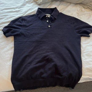 Marin blå pikétröja från These Glory Days - Säljer en stilren svart pikétröja från These Glory Days i silkblandning. Perfekt för en avslappnad men ändå elegant look. Säljer den då jag behöver pengarna 