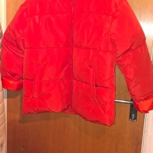 Röd pufferjacka - Ny oanvänd Snygg röd pufferjacka i 100% polyester. Jackan har en dragkedja framtill och är perfekt för kyligare dagar. Den är långärmad och har en klassisk pufferdesign som ger både stil och värme.