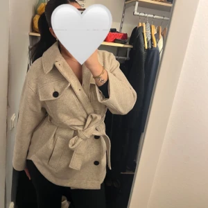 Beige kappa från ASOS - Säljer denna beige kappa med knappar och knytbälte i midjan. Kappan är från ASOS design i modellen petit storlek 34 men passar perfekt för alla (för referens är jag 170 och brukar använda storlek S/M)🩷 Denna jackan är perfekt för hösten då jackan har långa ärmar och en klassisk krage. Den är knappt använd och i mycket bra skick🩷