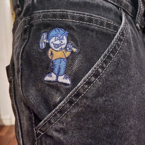 Svarta jeans med broderad detalj - Coola svarta jeans med en unik broderad figur på fickan. Man kan kalla det skate byxor och har en gul etikett med '93!' på baksidan.