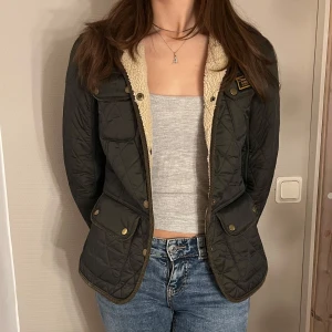 Grön quiltad jacka med teddyfoder - Säljer en snygg grön quiltad jacka från Barbour med mjukt teddyfoder. Jackan har långa ärmar och praktiska fickor med knappar☺️