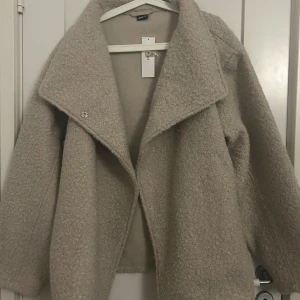 Beige teddyjacka från Gina Tricot - Mysig beige teddyjacka från Gina Tricot med bälte i midjan. Jackan har en stor krage och långa ärmar, perfekt för kyliga dagar. Den är i en mjuk och fluffig kvalitet. Storlek L men kan även användas som M. Aldrig använt, köpt för 599kr säljer för 500kr