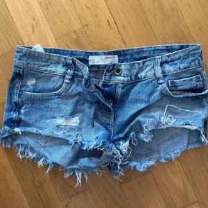 Blå jeansshorts från Zara - Snygga blå jeansshorts från Zara med slitna detaljer och fransig kant. Perfekta för sommardagar och ger en avslappnad look. De är lågmidjade och har klassiska femficksdesign. Låg midja!
