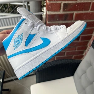 Nike Air Jordan 1 mid rise  - Snygga Nike Air Jordan sneakers i vitt med blå detaljer. Sparsamt anvönda! 