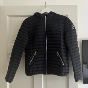 Svart dunjacka från Colmar - Snygg svart/blå dunjacka från Colmar med quiltad design och dragkedja framtill. Jackan har två praktiska fickor med dragkedjor och en diskret logga på ärmen. Perfekt för kyligare dagar. Är i väldigt bra skick, men har lite smink vid kragen som tas bort innan den säljs💞Storlek M i barnstorlek, men ungefär xs i vanlig