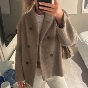 Arket Beige kappa med knappar - Säljer en stilren beige kappa med dubbelknäppning och stora knappar. Jackan har en klassisk design med lång ärm och är perfekt för höst och vår och vintern. Ny pris 2500kr
