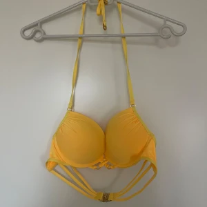Gul bikiniöverdel med knytband - Snygg gul bikiniöverdel med knytband i nacken och dekorativ detalj framtill. Perfekt för soliga dagar på stranden eller vid poolen. Justerbara axelband för bästa passform. Skulle tippa på den passar 75b och är med pushup