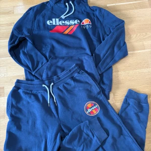 Blå hoodie och byxor från Ellesse - Säljer ett set med blå hoodie och matchande byxor från Ellesse. Hoodien har en stor logga på bröstet och dragsko i huvan. Byxorna har en logga på benet och resår i midjan. Perfekt för en avslappnad stil.