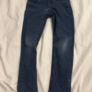 Blå skinny jeans för barn - Säljer ett par blå skinny jeans för barn i storlek 116. Jeansen har en klassisk design med fem fickor och är tillverkade i denim. Perfekta för vardagsbruk och ger en snygg och bekväm passform. De kommer tvättas och strykas innan de skickas! ⭐️