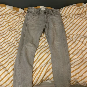 Grå jeans från Jack n Jones - Snygga grå jeans från Jack n Jones De har en knappgylf och fem fickor. Perfekta för en avslappnad stil. Det finns ett litet hål på högra benet, säljer för att jeansen är för små