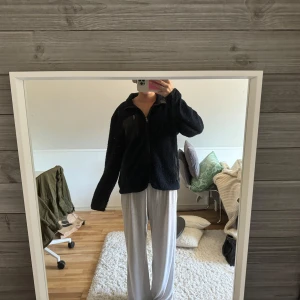 Svart teddyjacka med dragkedja - Mysig svart teddyjacka med dragkedja framtill. Perfekt för kyliga dagar med sin fluffiga och varma design. Jackan har en normal passform och långa ärmar.