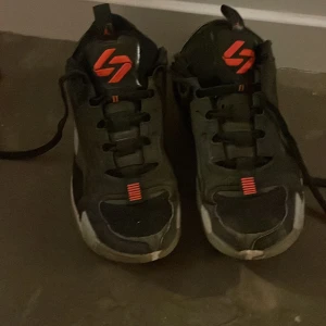 Svarta jordans med röda detaljer - Säljer ett par svarta jordans med röda detaljer och snörning. Skorna har en sportig design med vita sulor och är perfekta för vardagsbruk.
