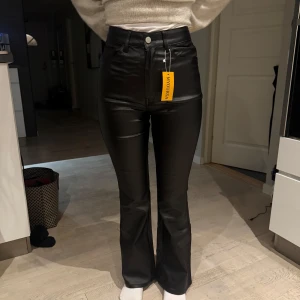 Svarta skinnbyxor - Snygga svarta skinnbyxor med hög midja och bootcut-stil. Perfekta för en trendig look med en tight passform som framhäver figuren. Byxorna har en dragkedja och knapp framtill. Stolek S.