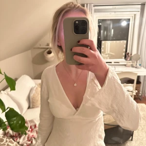 Vit omlottopp - Säljer en stilren vit omlottopp med långa ärmar. Toppen har en v-ringad design och är perfekt för en elegant look. Passar bra till både jeans och kjol.