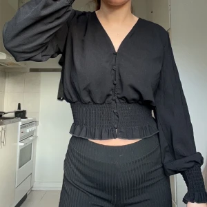 Svart blus med knappar - Snygg svart blus med knappar framtill och v-ringning. Den har långa ärmar och en smockad midja som ger en fin passform. Perfekt för både vardag och fest!