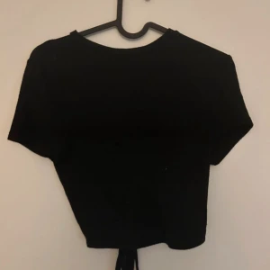 Svart kortärmad topp med öppen rygg - Säljer en snygg svart topp med korta ärmar. Den har en öppen rygg med cool snörning som ger en unik look. Perfekt för fest eller en utekväll!🥳