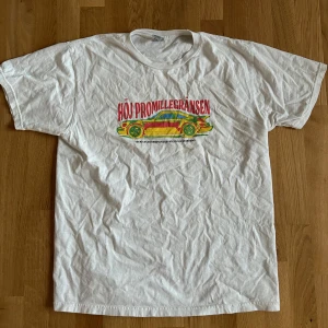 Vit t-shirt med tryck - Säljer en vit t-shirt med ett färgglatt tryck av en bil och texten 'Höj promillegränsen'. Perfekt för en avslappnad stil T-shirten är i bra skick och passar till vardags.