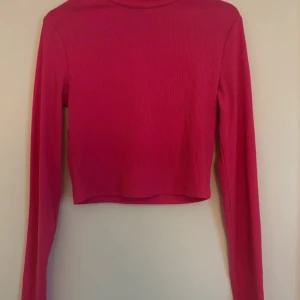 Rosa croppad tröja - Säljer en superfin rosa polotröja som är ribbad och har långa ärmar. Perfekt för höst och vår när det är lite kyligt ute. Tröjan är croppad och ger en snygg look till både jeans och kjol. Den är i bra skick och redo för en ny ägare!
