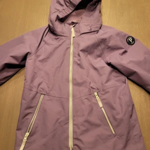 Lila jacka från Polarn O. Pyret - Säljer en superfin lila jacka från Polarn O. Pyret i storlek 134. Den har en praktisk huva och dragkedjor i kontrasterande färg. Perfekt för vår och höst! Jackan är i mycket bra skick och redo för nya äventyr.