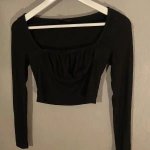 Svart ribbad croppad topp - Snygg svart ribbad topp med långa ärmar och en croppad passform. Perfekt för både vardag och fest. Toppen har en stilren design med en lätt rynkad detalj framtill som ger en extra touch. (PM OM DU VILL HA FLER BILDER)