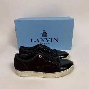Lanvin skor  - Säljer ett par snygga vinröda sneakers från Lanvin. De har en glansig tå och snörning framtill. Skorna är i bra skick med lite slitage på sulorna. Perfekta för både vardag och fest! Uk5 passar 40