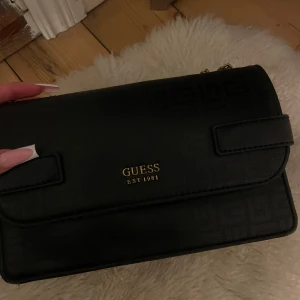 Svart axelväska från Guess - Snygg svart axelväska från Guess med guldfärgade kedjehandtag! Kedjan kan justeras! Hör av er för fler bilder🖤kan gå ner i pris vid snabb affär 