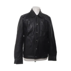 Svart skinnjacka från Tiger of Sweden - Säljer en stilren svart skinnjacka från Tiger of Sweden i storlek medium. Jackan har en klassisk design med knappar framtill och är tillverkad i 100% kalvskinn. Perfekt för höst och vår, och ger en cool look till vilken outfit som helst. Passar som både jacka och overshirt. Har ett litet slitage på framsidan (se bild) men inget som syns på håll. 