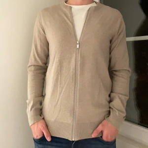 Beige kofta från Lindbergh - Tja! Säljer nu denna stilrena kofta från Lindbergh i storlek S. Den har en dragkedja framtill och är i ett mjukt material som passar perfekt för både vår och höst. Tröjan är använd ett fåtal gånger men kommer utan defekter! Modellen på bilden är 182 cm och koftan är lite tajt för mig. Nypris: 799 kr, mitt pris: 199. Priset är diskutabelt, hör gärna av er vid frågor!