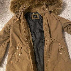 Brun parkajacka från Reserved - Säljer en snygg brun parkajacka från Reserved i storlek 38. Jackan har en mysig fuskpäls på huvan och praktiska dragkedjor på fickorna. Perfekt för höst och vinter med sin varma och tåliga design. Passar både till vardags och lite finare tillfällen. 🧥🍂