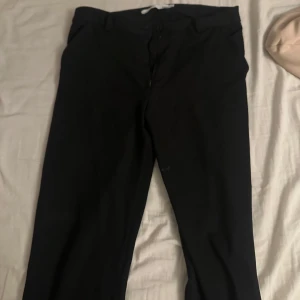 Svarta kostymbyxor - Säljer ett par stilrena svarta kostymbyxor från 157 i storlek S. Byxorna har en klassisk design med dragkedja och knapp framtill. Perfekta för både formella tillfällen och vardagsbruk. De är i mycket bra skick och redo för en ny ägare!