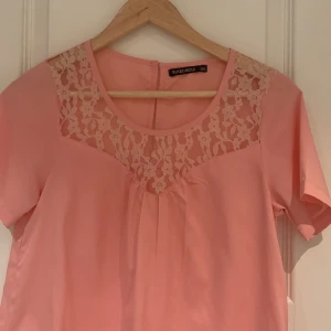 Rosa topp med spetsdetaljer från Rut&Circle - Söt rosa topp från Rut&Circle i storlek 34. Den har korta ärmar och en vacker spetsdetalj vid halsringningen som ger en romantisk touch. Perfekt för vår och sommar! 💖