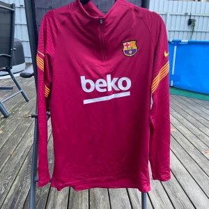 Röd långärmad Barcelona-tröja - Säljer en snygg röd långärmad Barcelona-tröja från Nike. Perfekt för fotbollsträning eller som en casual look. Tröjan har klubbens emblem på bröstet och Beko-loggan tryckt på framsidan. Den har en halv dragkedja vid halsen. Passar perfekt för höst och vår! Använd ungefär 2 gånger då den är förstor 